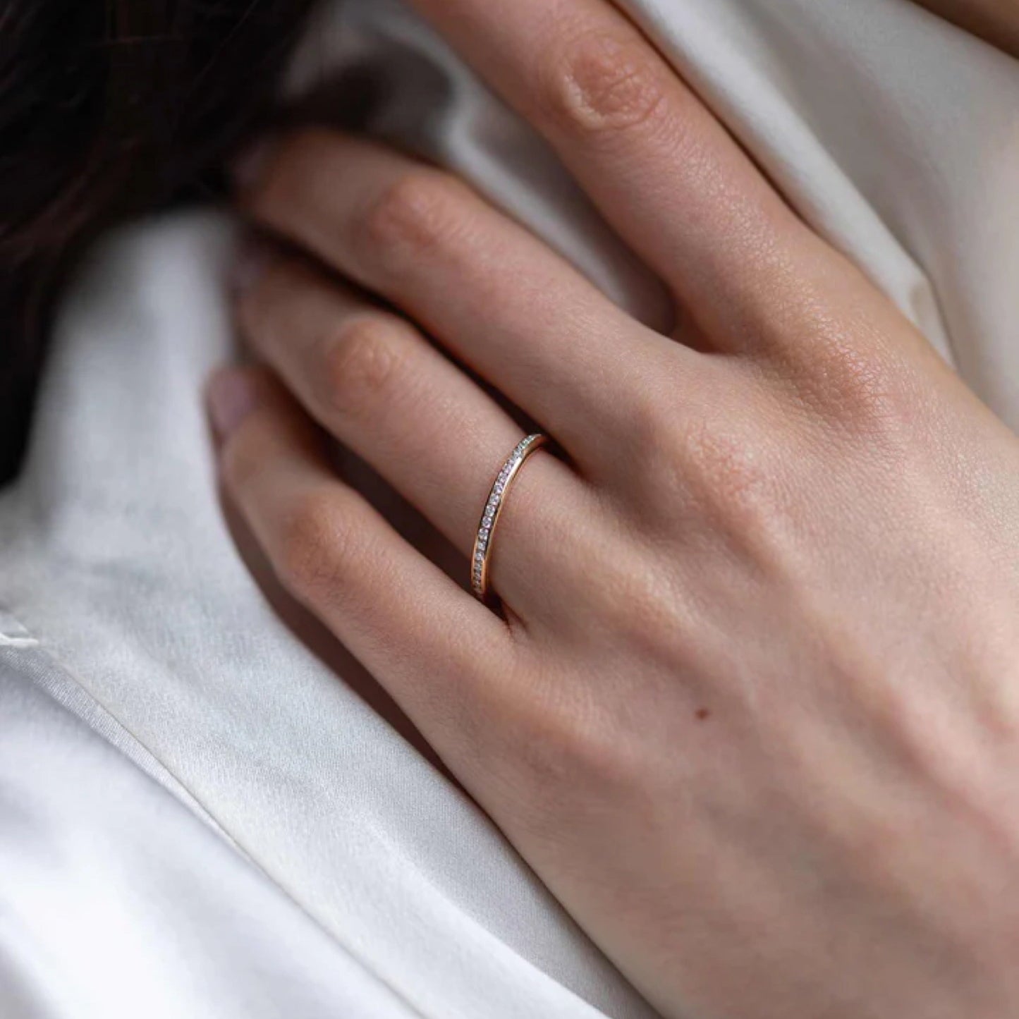 Elegant hand wearing a 0.35 TCW round cut diamond wedding band on a satin background.